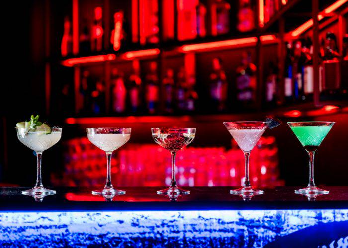 A selection of fancy cocktails on a bar with a red neon background.